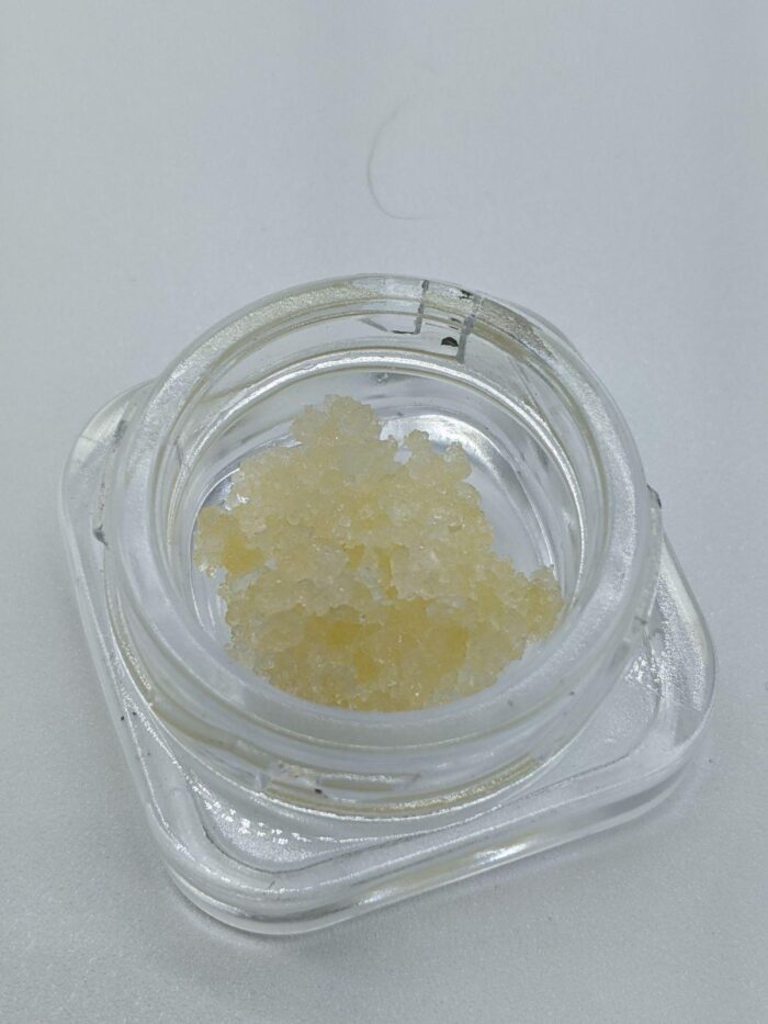 Close-up of THC Diamonds concentrate in a glass jar, showcasing its crystal-like structure and purity for potent cannabis experiences.